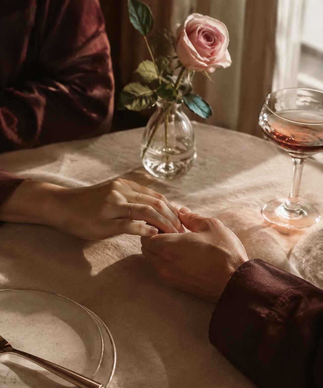 Two hands meeting across a café table beside a blush rose